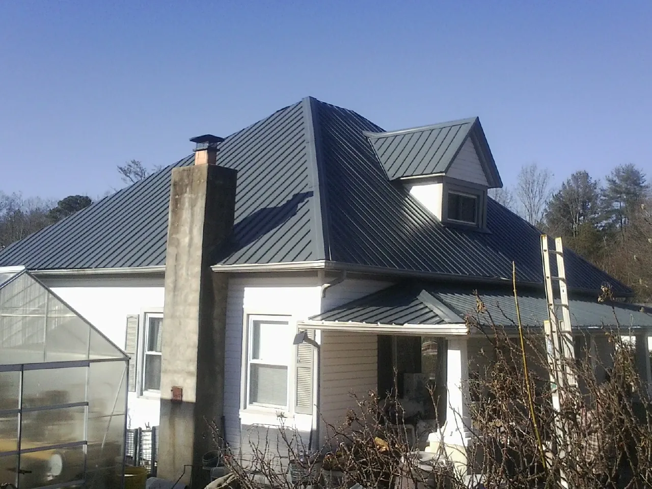 Dark blue standing seam metal roof on a white farmhouse with dormer — Slate & Tile Roof Repair by Roofing Brothers in Lacona