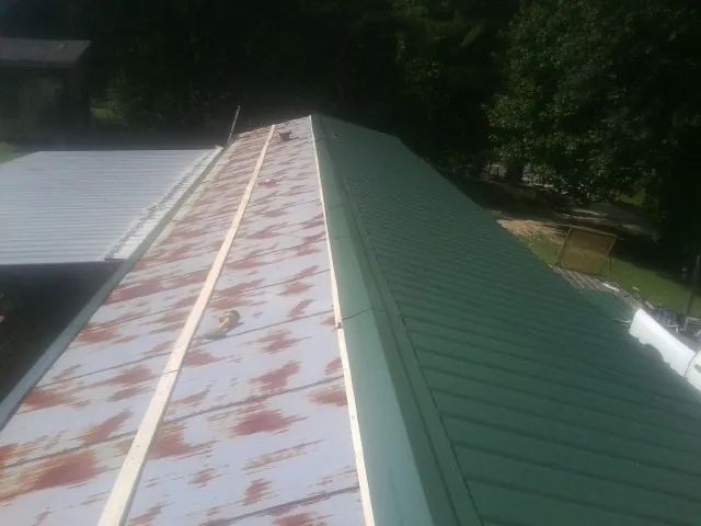 Old rusted panels beside newly installed green metal roofing — Wind Damage Roof Repair by Roofing Brothers in Lacona