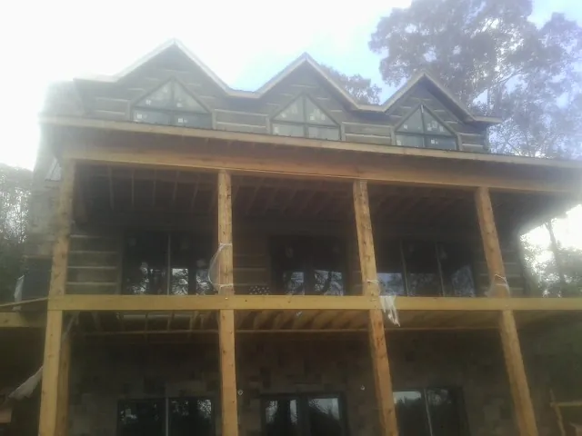 Dormers and porch framing on a large log home under construction — Roof Coating work by our crew in Lacona
