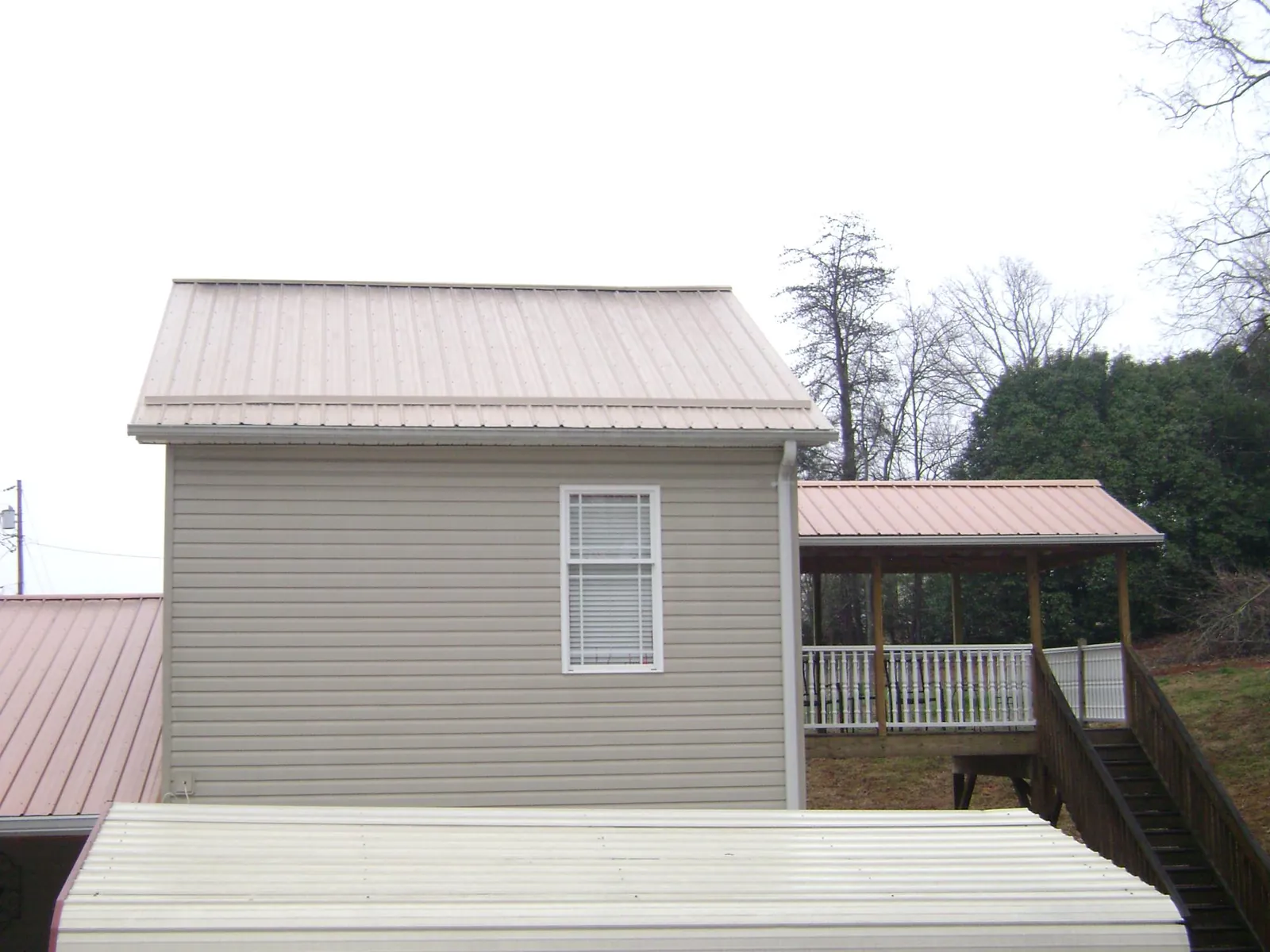 Tan metal roofs on a two story addition and attached porch, from a Roof Replacement job in Lacona