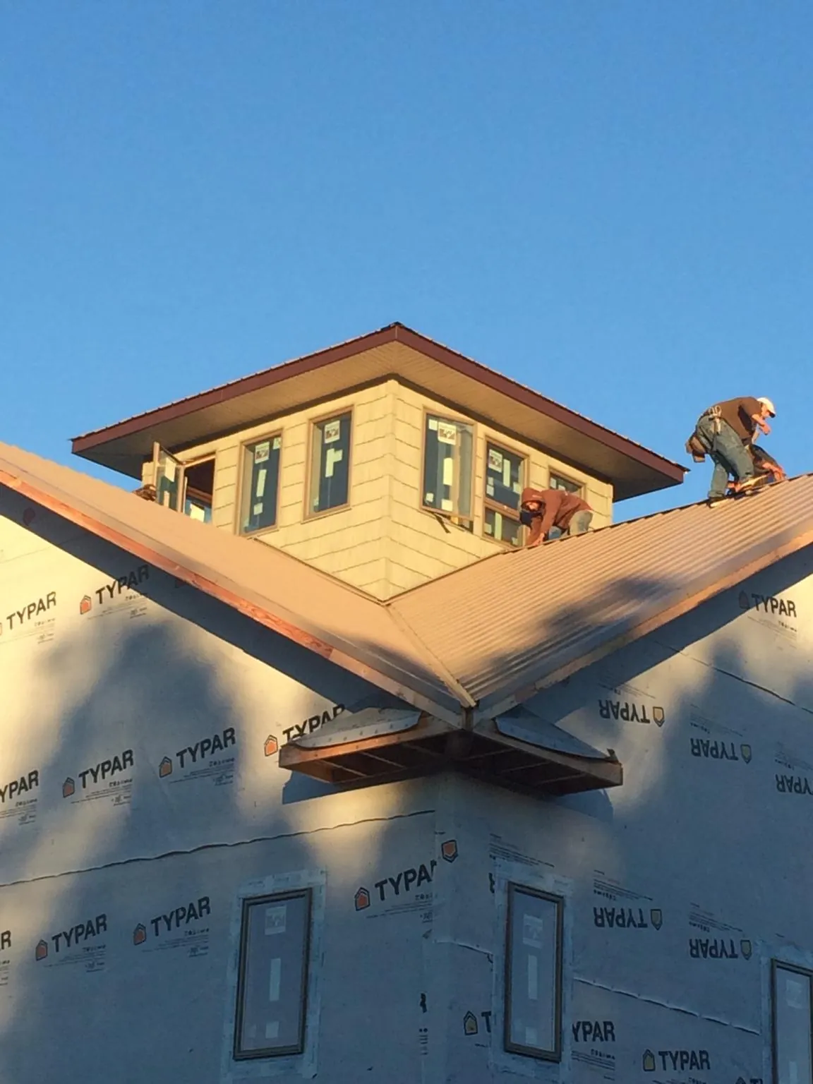 Roofers working around a rooftop cupola on a new metal roof at sunset — Roof Waterproofing in Lacona by Roofing Brothers